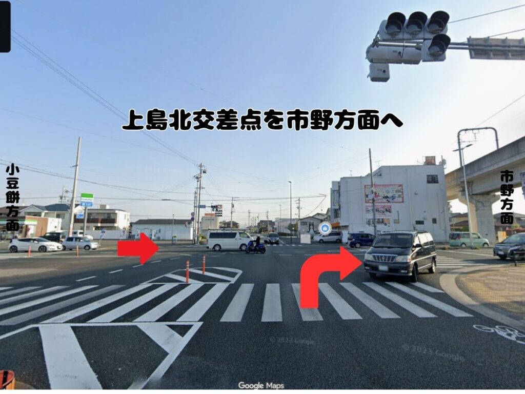 ドッグアシルへのアクセス案内。上島北交差点を右折(または直進方向)して市野方面へ進む経路を、赤い矢印で示した道路の風景写真。