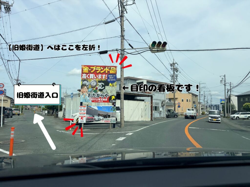 ドッグアシルへのアクセス案内。「おたからや」の大きな看板がある三差路の交差点を、白い矢印に沿って左折して旧姫街道入口へ進むルートを示した道路写真。
