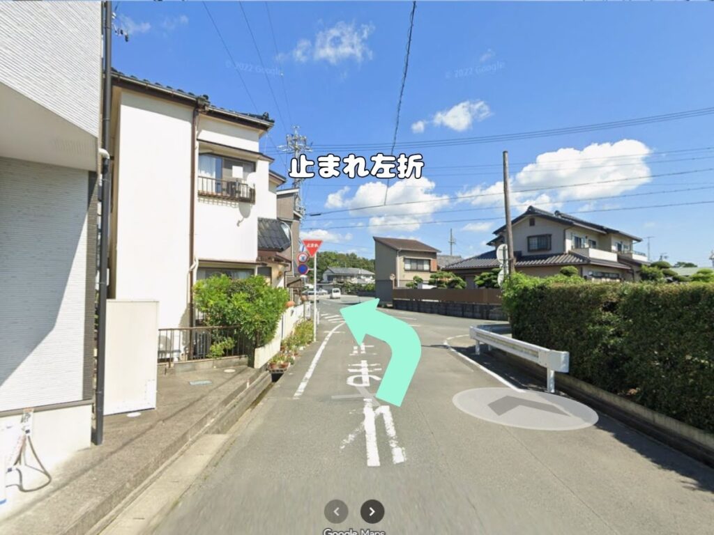 トリミングサロン「ドッグアシル」からの帰り道案内。「突き当りを左折」のテロップが入り、正面に白いガードレールと土手がある丁字路をミントグリーンの矢印に従って左折する風景写真。