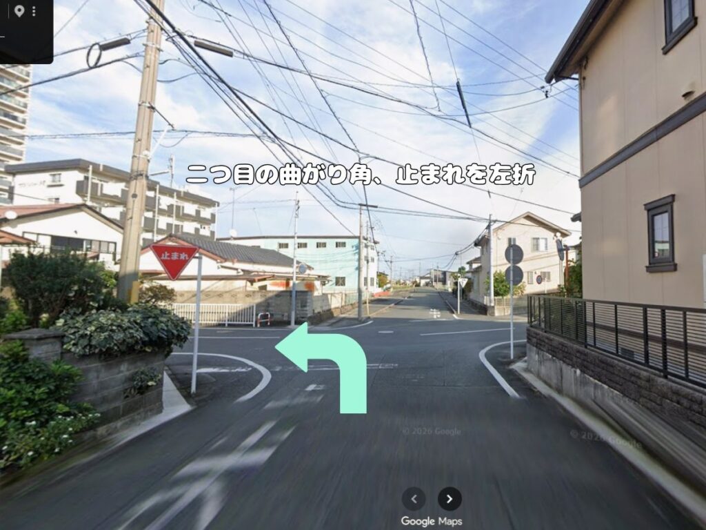 トリミングサロン「ドッグアシル」からの帰り道案内。「二つ目の曲がり角、止まれを左折」のテロップが入り、左側にある赤い一時停止標識の手前をミントグリーンの矢印に従って左折する風景写真。