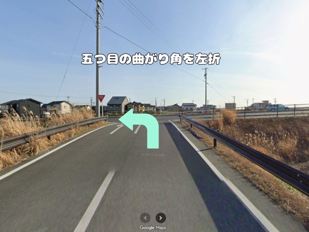 トリミングサロン「ドッグアシル」へのアクセス案内。「五つ目の曲がり角を左折」のテロップが入り、ガードレールに囲まれた上り坂の突き当たりをミントグリーンの矢印に従って左折する風景写真。