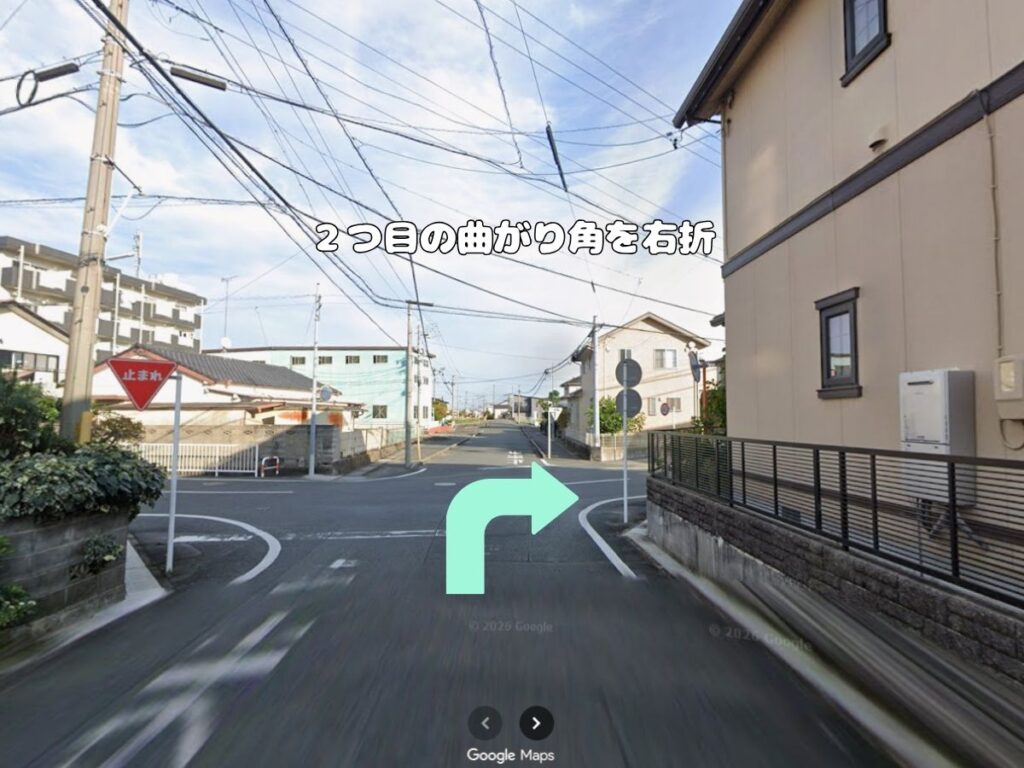 トリミングサロン「ドッグアシル」へのアクセス案内。「2つ目の曲がり角を右折」のテロップが入り、左側に「止まれ」の標識がある交差点をミントグリーンの矢印に従って右折する道路の風景写真。